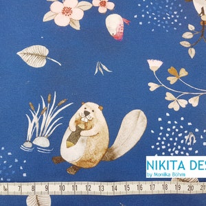 Könnte beinhalten: Blauer Stoff mit einem sich wiederholenden Muster aus einem Biber, der einen Ast hält, einem Vogel, Blumen und Blättern. Der Stoff hat unten ein weißes Maßband mit dem Text "NIKITA DESIGN by Monika Böhm".