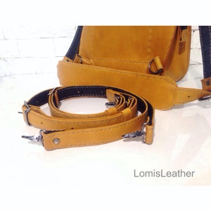Puede incluir: Un primer plano de una mochila de cuero amarilla con correas ajustables. Las correas son de cuero y tienen una inserci&oacute;n de cinta negra. La mochila tiene un dise&ntilde;o simple y es perfecta para el uso diario.