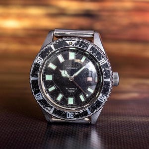 Puede incluir: Un reloj de pulsera plateado vintage con esfera negra y marcadores luminosos. La esfera muestra la marca "CREENE" y "AUTOMATIC". El bisel tiene un aspecto desgastado y texturizado. Un reloj cl&aacute;sico.