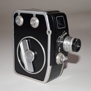 Puede incluir: Una cámara de cine vintage en blanco y negro con una lente y diales prominentes. La cámara tiene un elemento de diseño circular en la parte delantera y la palabra "Jupiter" está escrita en el lateral. Un equipo de fotografía clásico.