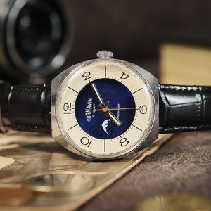 May include: A vintage wristwatch with a silver-toned case and a black leather band. The watch face features a cream-colored outer ring with black numerals and a deep blue center with the brand name "Cornavin". The watch is displayed on a textured surface.