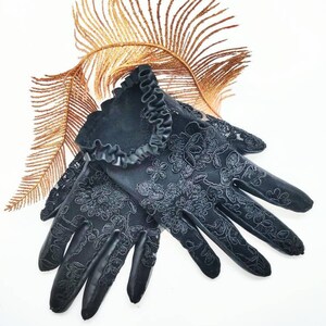 May include: A pair of black lace gloves with a ruffled trim. The gloves feature a floral pattern and are made from a delicate fabric.