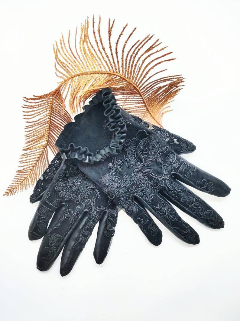 May include: A pair of black lace gloves with a ruffled trim. The gloves feature a floral pattern and are made from a delicate fabric.