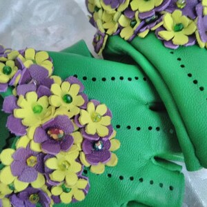 May include: Green leather fingerless gloves with purple and yellow flower embellishments. The flowers are made of leather and have green beads in the center.