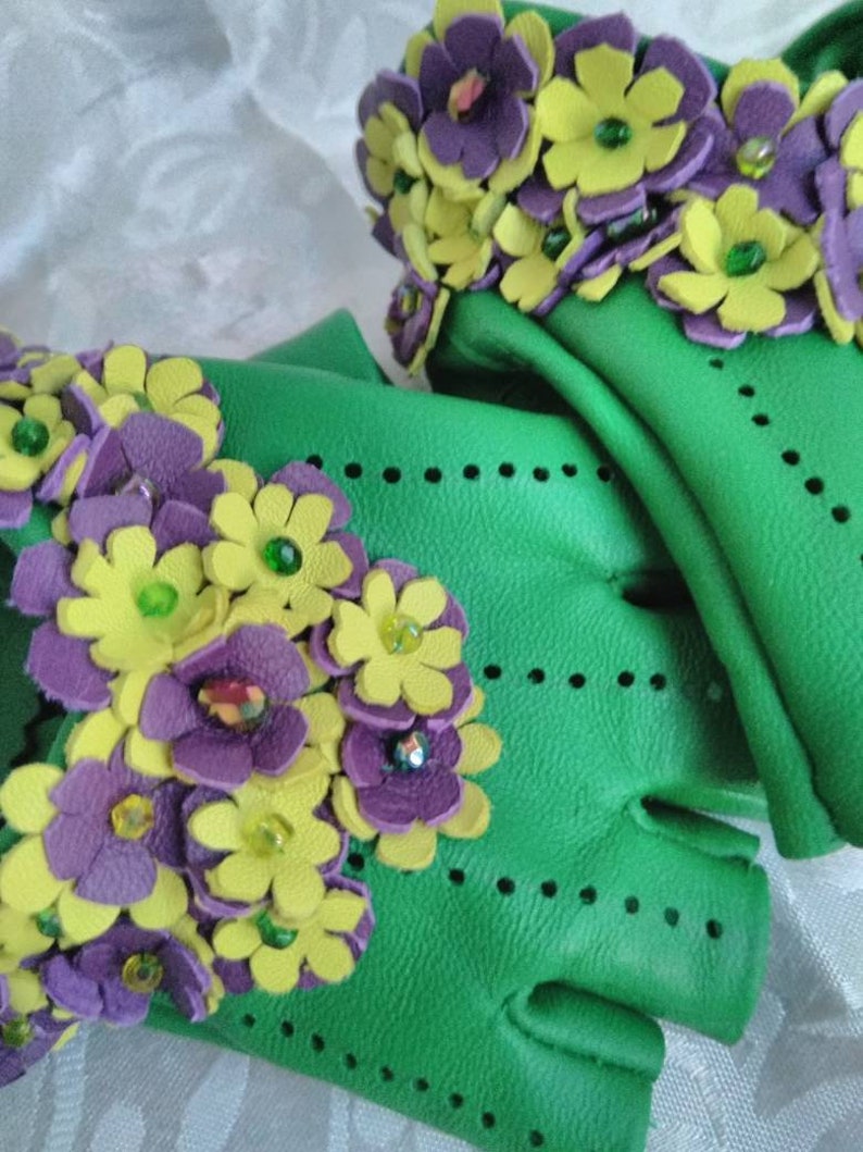 May include: Green leather fingerless gloves with purple and yellow flower embellishments. The flowers are made of leather and have green beads in the center.