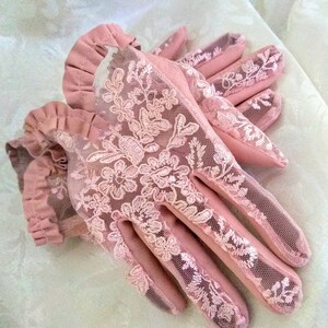 May include: A pair of pink lace gloves with a ruffled cuff. The gloves are made of a delicate fabric with a floral pattern.