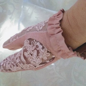 May include: A pair of pink fingerless gloves with a delicate lace design. The gloves have a ruffled edge and are made of a soft, sheer fabric.