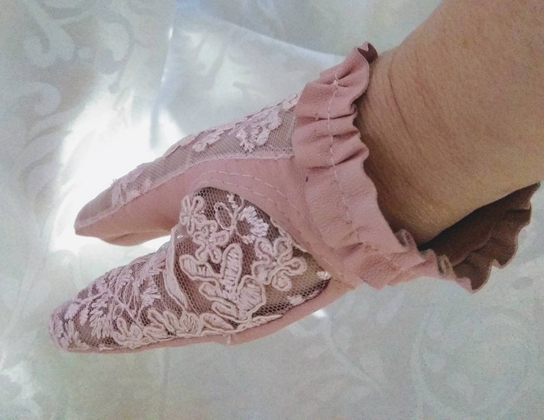 May include: A pair of pink fingerless gloves with a delicate lace design. The gloves have a ruffled edge and are made of a soft, sheer fabric.