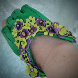 May include: Green leather fingerless gloves with a decorative trim of yellow and purple flowers with green and iridescent beads.