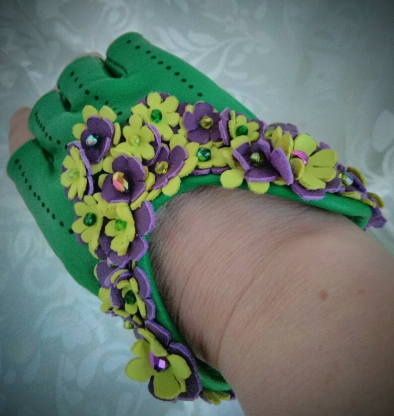 May include: Green leather fingerless gloves with a decorative trim of yellow and purple flowers with green and iridescent beads.