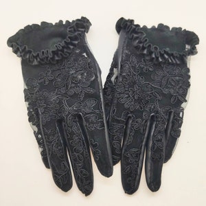 May include: A pair of black lace gloves with a ruffled trim. The gloves feature a floral pattern and are made from a sheer fabric.
