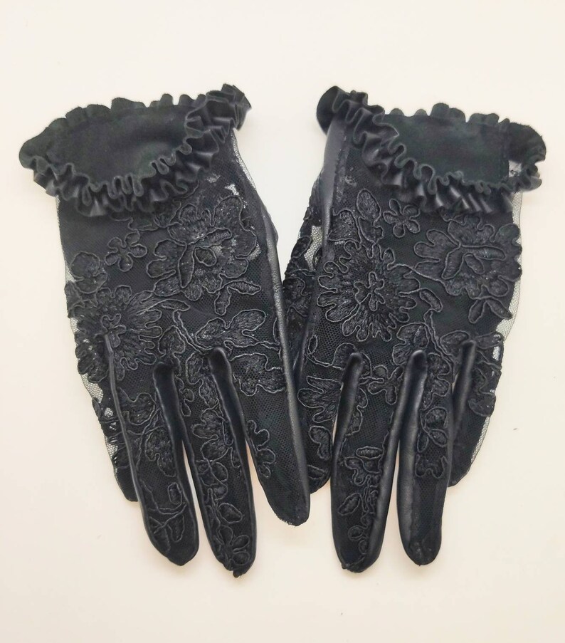 May include: A pair of black lace gloves with a ruffled trim. The gloves feature a floral pattern and are made from a sheer fabric.