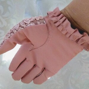 May include: A pair of pink leather gloves with a lace detail on the back of the hand and a ruffled cuff.