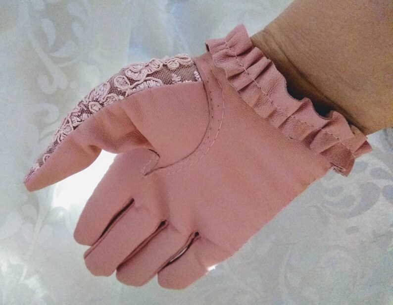 May include: A pair of pink leather gloves with a lace detail on the back of the hand and a ruffled cuff.