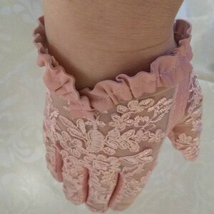 May include: A pair of pink lace gloves with a ruffled trim. The gloves are made of delicate lace and have a floral pattern.