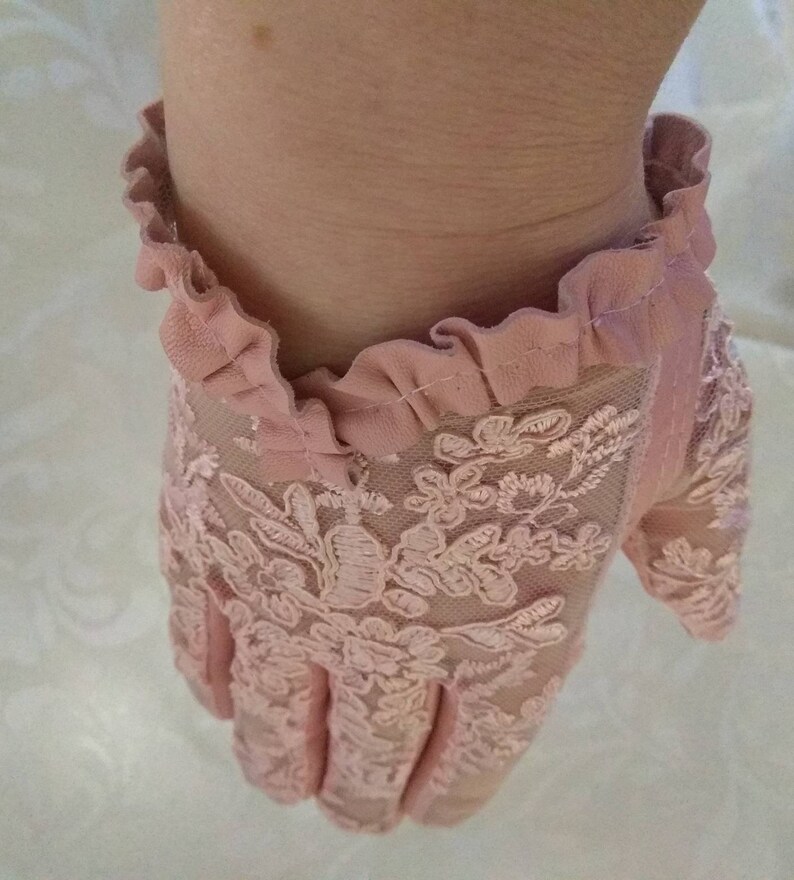 May include: A pair of pink lace gloves with a ruffled trim. The gloves are made of delicate lace and have a floral pattern.