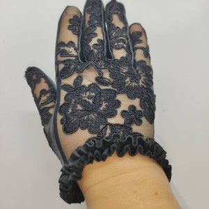 May include: Black lace gloves with a ruffled wristband. The gloves feature a floral design.