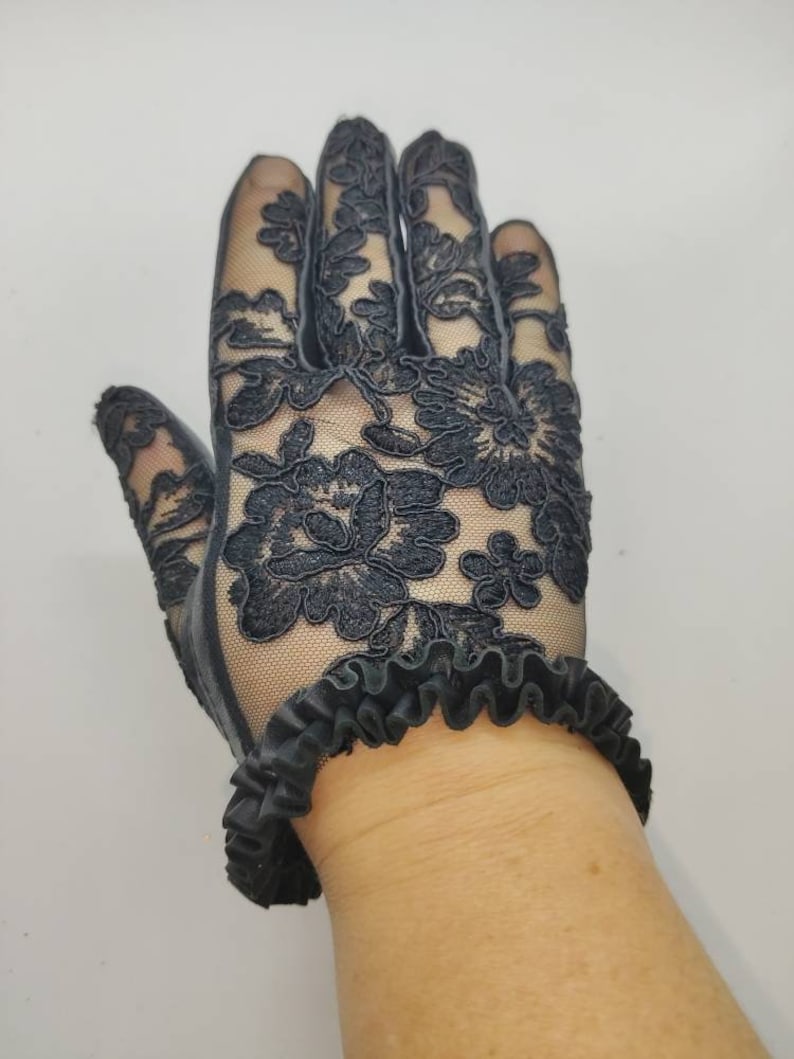May include: Black lace gloves with a ruffled wristband. The gloves feature a floral design.