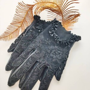 May include: Black lace gloves with a frilled trim. The gloves feature a floral pattern and are made from a delicate fabric.