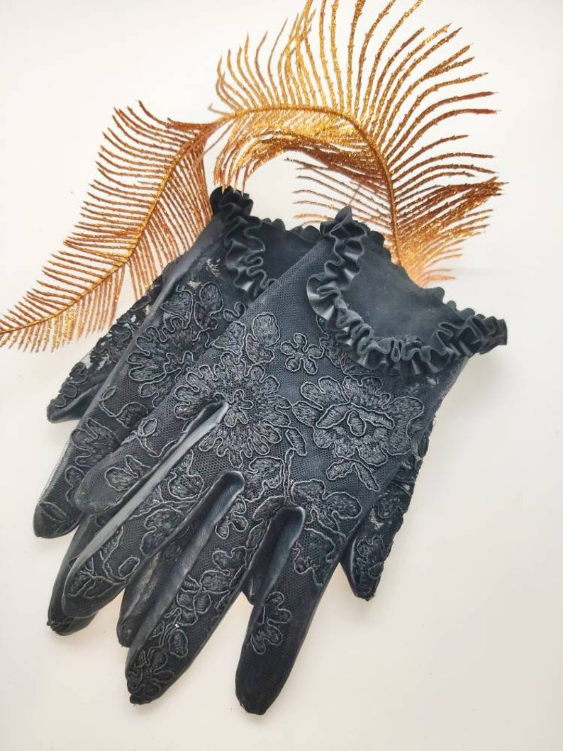 May include: Black lace gloves with a frilled trim. The gloves feature a floral pattern and are made from a delicate fabric.