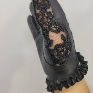 May include: Black leather gloves with a lace detail on the back of the hand and a ruffled trim at the wrist.