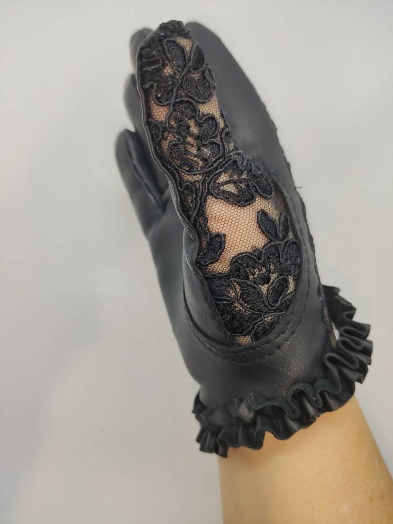 May include: Black leather gloves with a lace detail on the back of the hand and a ruffled trim at the wrist.