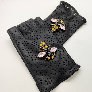 May include: Black leather fingerless gloves with a pink and gold bee embellishment on each glove.