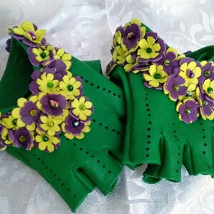 May include: A pair of green fingerless gloves with purple and yellow felt flowers and beads.