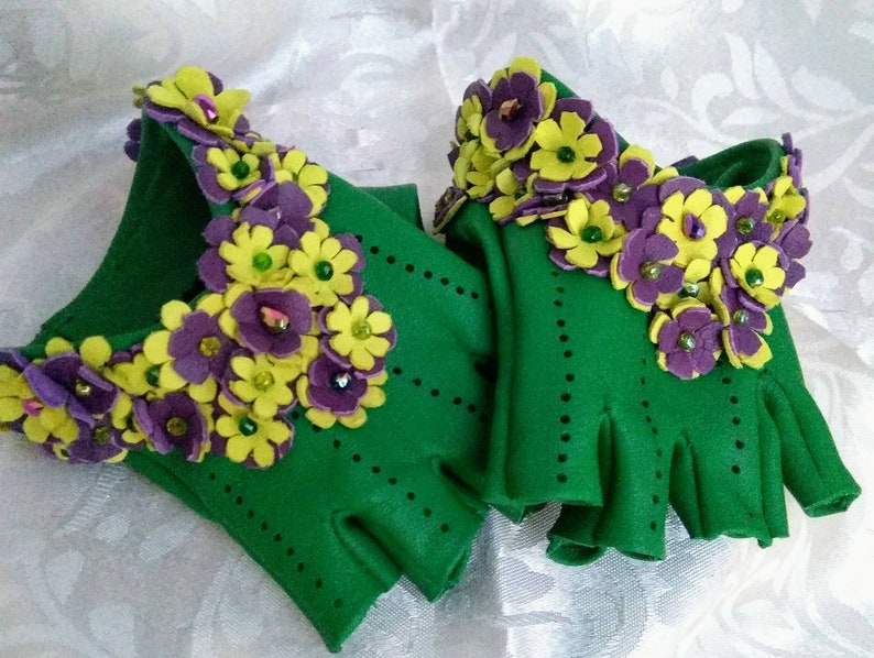 May include: A pair of green fingerless gloves with purple and yellow felt flowers and beads.