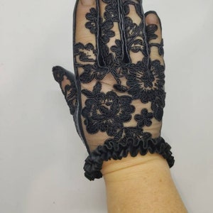 May include: Black lace gloves with a ruffled cuff. The gloves are made of a delicate, sheer fabric with a floral pattern.