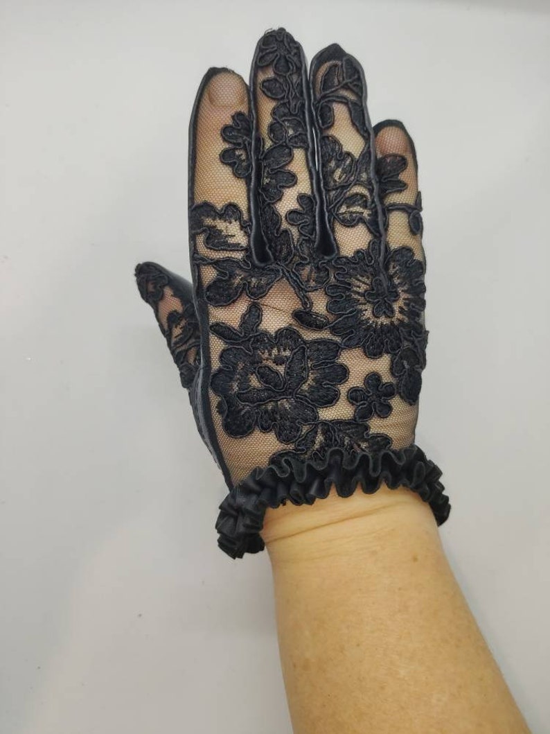 May include: Black lace gloves with a ruffled cuff. The gloves are made of a delicate, sheer fabric with a floral pattern.