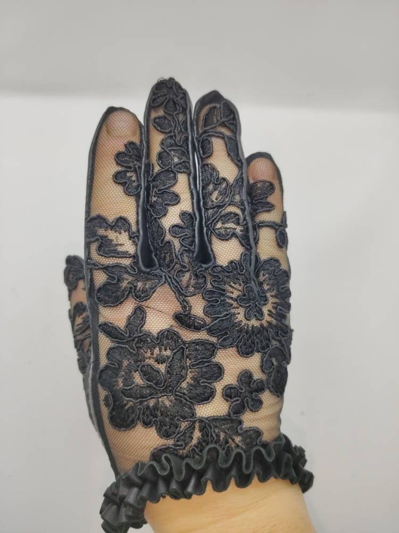 May include: Black lace gloves with a floral design. The gloves have a ruffled cuff.