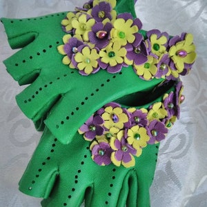 May include: Green leather fingerless gloves with yellow and purple flower embellishments. The flowers are made of leather and have small beads in the center.