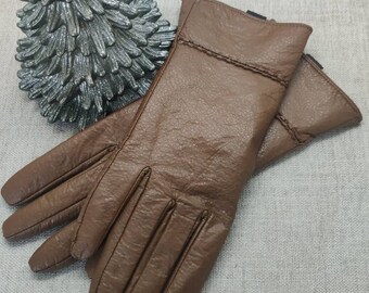 May include: A pair of brown leather gloves with a textured finish. The gloves are folded in half and the fingertips are visible.