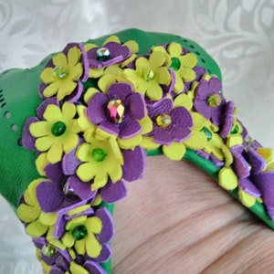 May include: Green leather bracelet with purple and yellow leather flowers embellished with green and iridescent rhinestones.