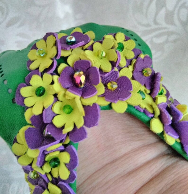 May include: Green leather bracelet with purple and yellow leather flowers embellished with green and iridescent rhinestones.