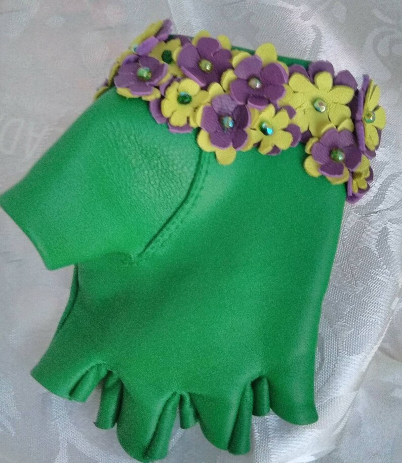 May include: Green leather fingerless gloves with a decorative trim of purple and yellow flowers with green rhinestones.