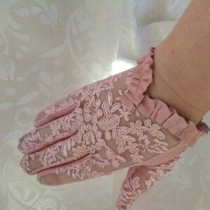 May include: A pair of pink lace gloves with a ruffled edge. The gloves are delicate and feminine.