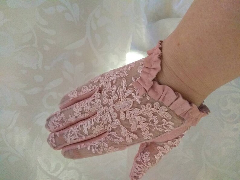 May include: A pair of pink lace gloves with a ruffled edge. The gloves are delicate and feminine.