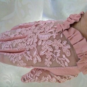 May include: A pair of pink lace gloves with a ruffled edge. The gloves are made of a delicate, sheer fabric with a floral pattern.