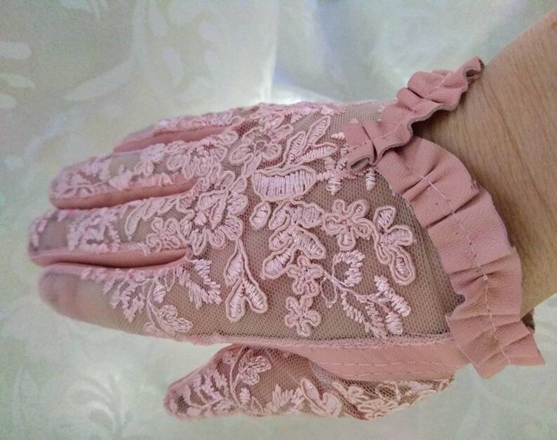 May include: A pair of pink lace gloves with a ruffled edge. The gloves are made of a delicate, sheer fabric with a floral pattern.