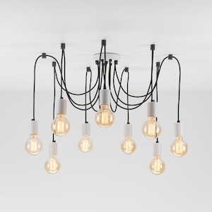 May include: A modern chandelier with ten Edison-style light bulbs. The bulbs are suspended from the ceiling by black cords and white fixtures. The light bulbs are a warm yellow color, and the fixture is against a white background.