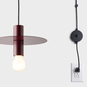 May include: A red pendant light with a round, flat shade and a black cord. The light is plugged into a wall outlet and has an in-line switch.