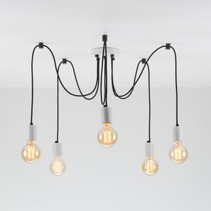 May include: A modern, multi-light pendant lamp with six Edison-style bulbs. The fixture features black cords, white cylindrical bulb holders, and a white ceiling plate. The bulbs emit a warm, inviting glow, perfect for a contemporary interior.