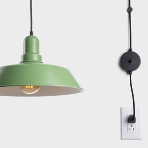 Könnte beinhalten: Eine grüne Pendelleuchte mit schwarzem Kabel und Stecker. Die Leuchte hat ein klassisches, industrielles Design mit rundem Schirm und sichtbarer Glühbirne. Das Licht ist von der Decke abgehängt.