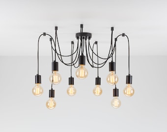 Puede incluir: Una lámpara colgante negra con varias luces y diez bombillas expuestas de estilo Edison. Las bombillas son de tonos cálidos y están encerradas en casquillos cilíndricos negros. La lámpara está montada en un techo blanco.