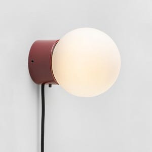 Peut inclure: Un luminaire mural rouge avec un globe en verre dépoli blanc. Le luminaire est doté d'un cordon noir.