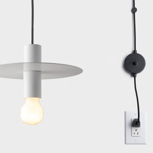 Op de afbeelding: Een witte hanglamp met een ronde, platte kap en een wit snoer. De lamp is aangesloten op een stopcontact en heeft een schakelaar in het snoer.