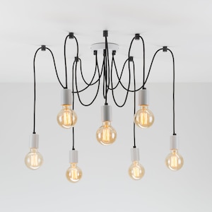 May include: A modern ceiling light fixture with eight Edison-style bulbs. The bulbs hang from black cords attached to the ceiling. Each bulb is encased in a white and gray cylindrical holder. The light bulbs are lit with a warm glow.