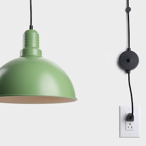 May include: A green pendant light with a dome-shaped shade and a black cord. The light is plugged into a white wall outlet. The light fixture has a classic, industrial design.